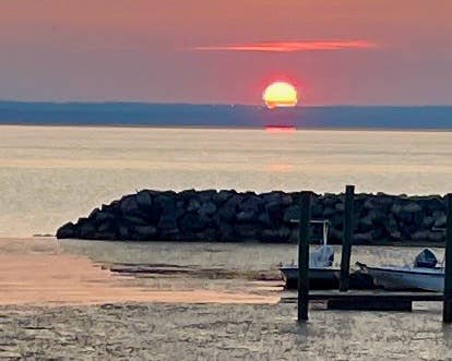 The sun sets over the Chesapeake Bay with a small dock and a couple of boats in the foreground.